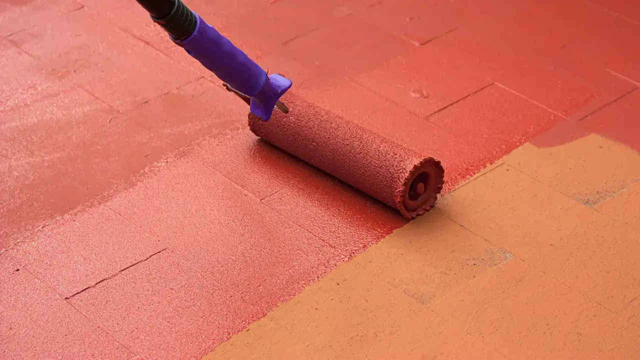 Rodillo pintando suelo de patio exterior con pintura roja, renovando el espacio.