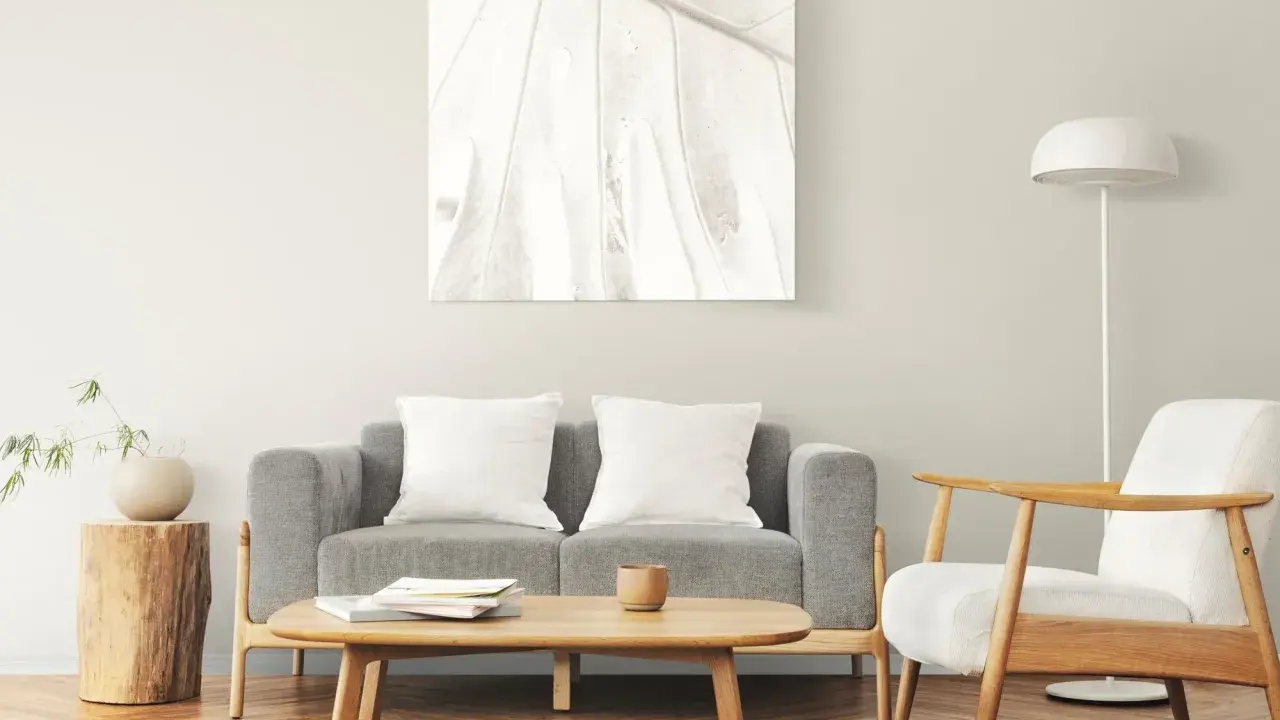 Un cuadro de hoja en tonos claros decora la pared, complementando el estilo zen de los cuadros feng shui dormitorio. Sofá gris, sillón blanco y mesa de centro de madera.