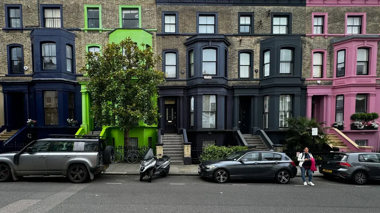 Fila de casas de colores vibrantes en Londres, con fachadas azules, verdes y rosas, estacionadas junto a coches y una moto.