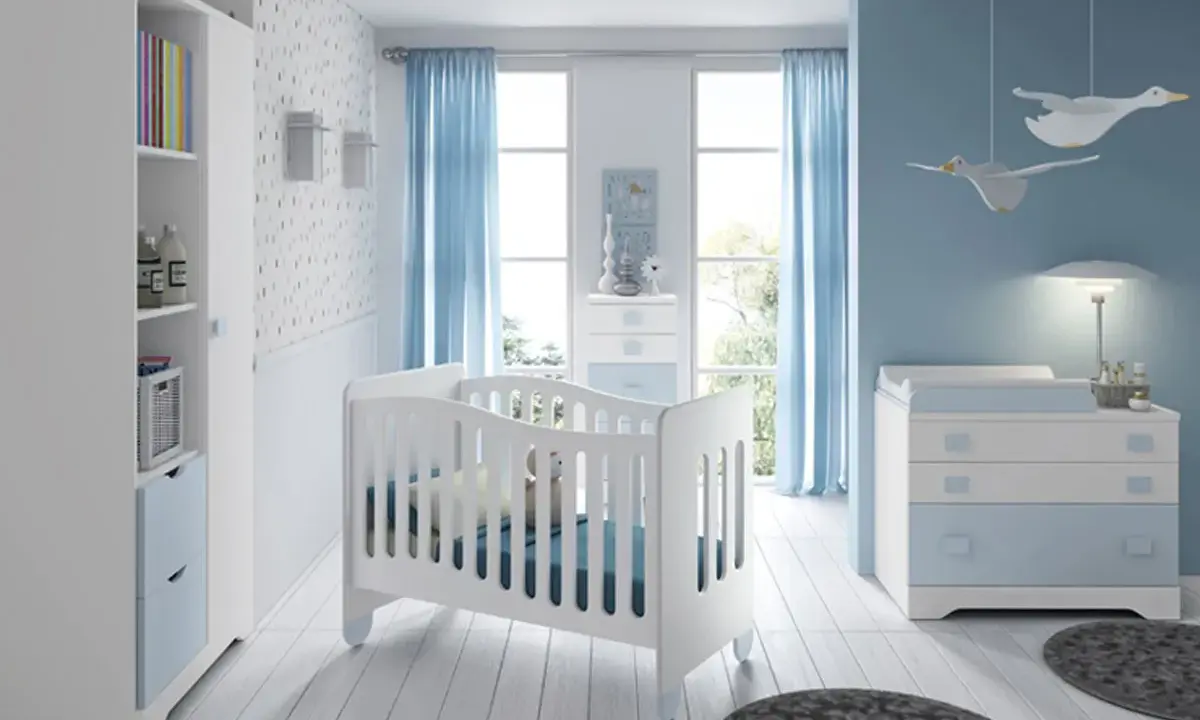 Habitación de bebé con cuna blanca, cómoda azul y estantería. Los colores para habitación de bebé son serenos, con predominio del azul y blanco.