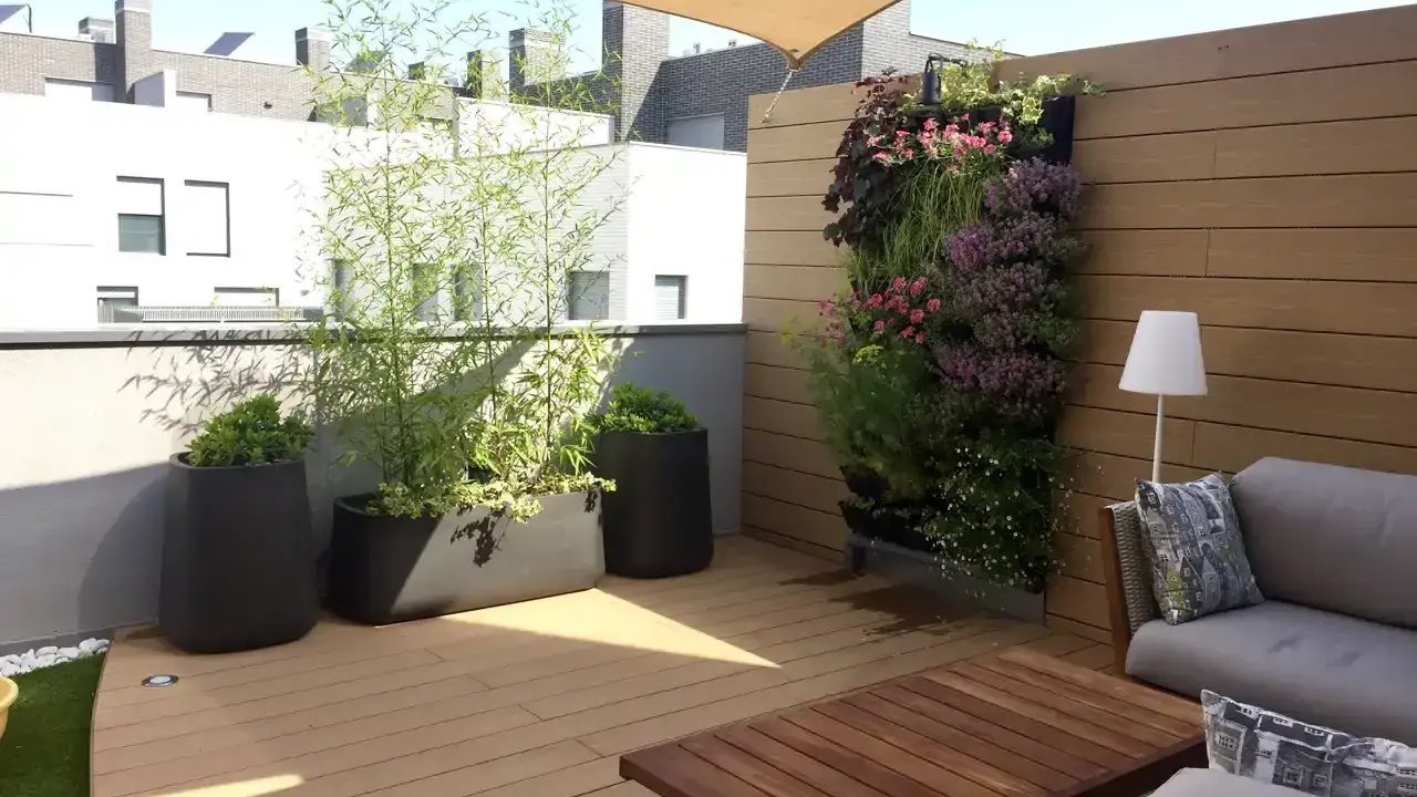 Un **jardín moderno** en una terraza con sofá, mesa de madera, plantas en macetas y un muro verde vibrante.
