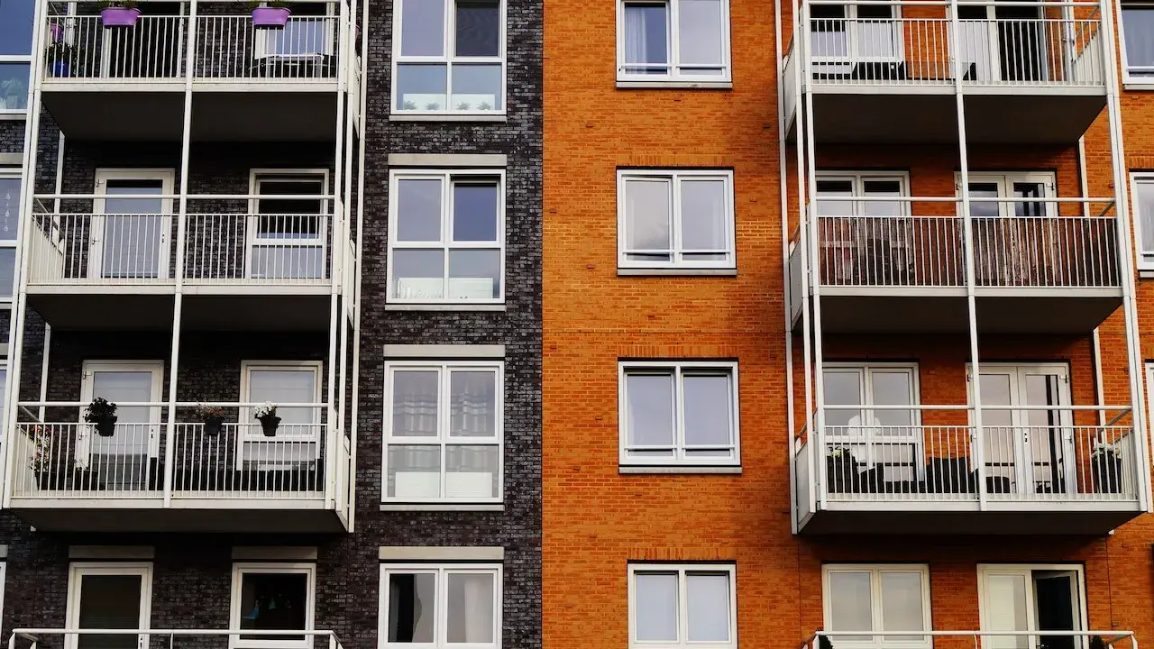 Fachada de edificio moderno con ladrillo naranja y oscuro, balcones blancos y ventanas. Un proyecto de reforma fachada casa que realza su estética.