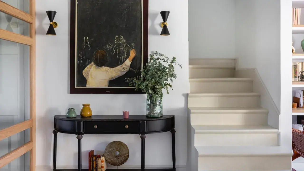 Entrada de una casa pequeña con consola negra, cuadro de tiza y escaleras. Un toque de feng shui casa pequeña para armonizar el espacio.