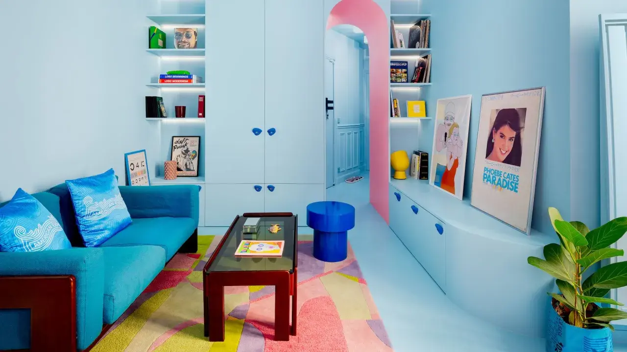 Salón pequeño con sofá azul, alfombra geométrica y estanterías llenas de objetos. Los colores pastel y vibrantes son ideales como colores para pintar salones pequeños.