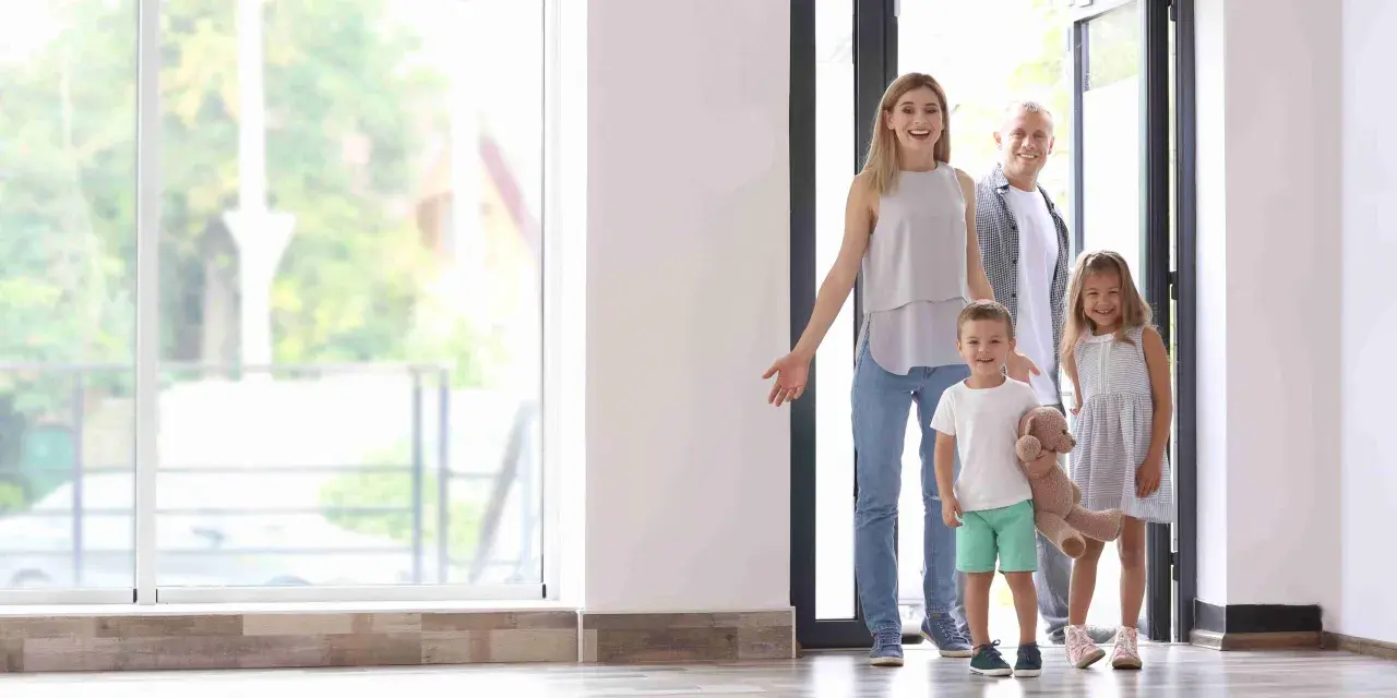 Familia de 4 miembros sonriendo y entrando a su nuevo hogar, pensando en el consumo medio electricidad.