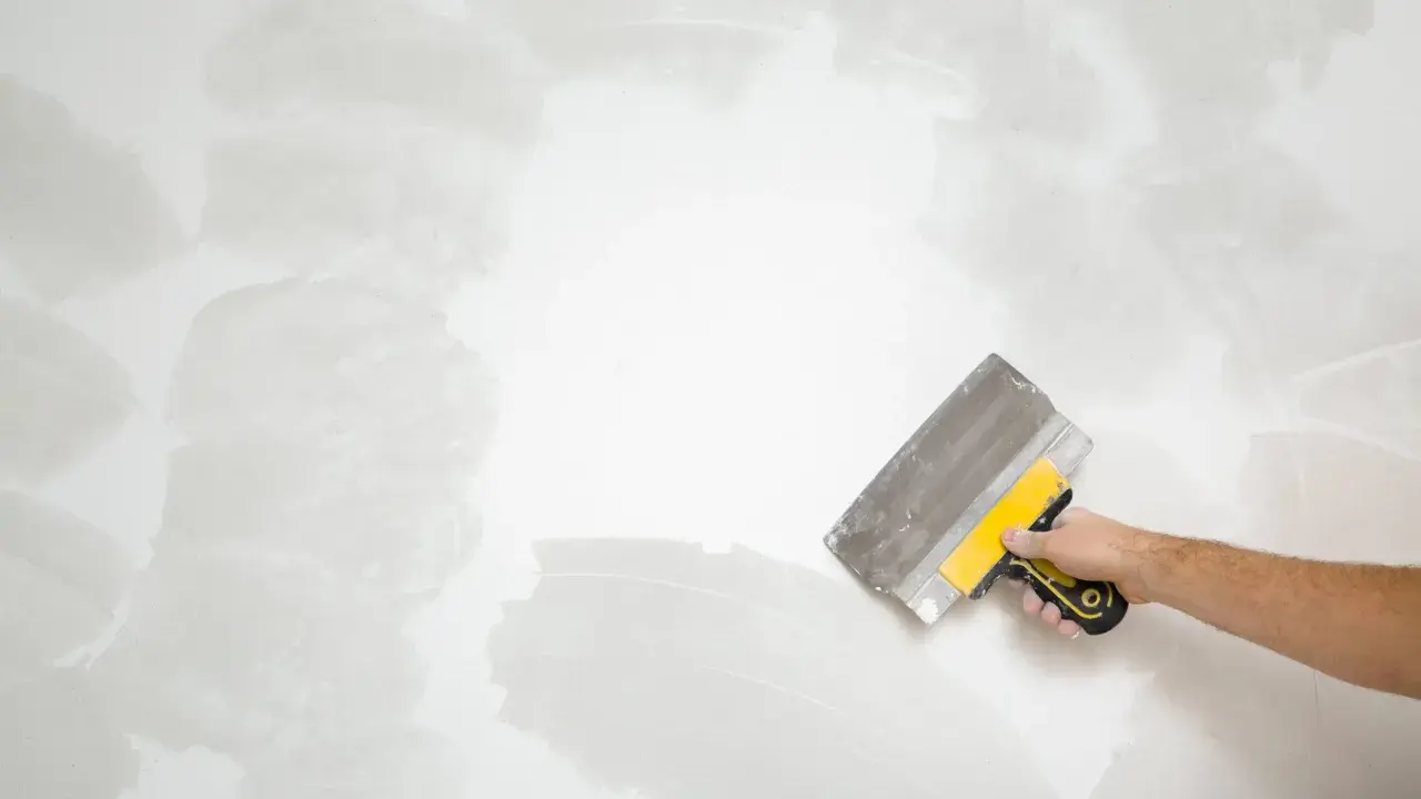 Mano con espátula trabajando en pared rugosa, como quitar pintura.