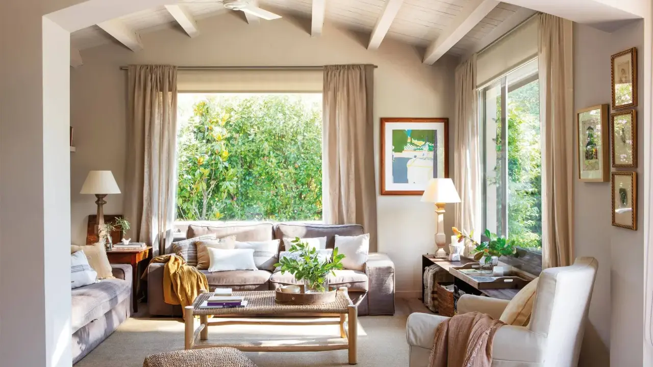 Salón acogedor con sofás en color greis, mesa de centro de madera y gran ventanal con vistas a la vegetación.