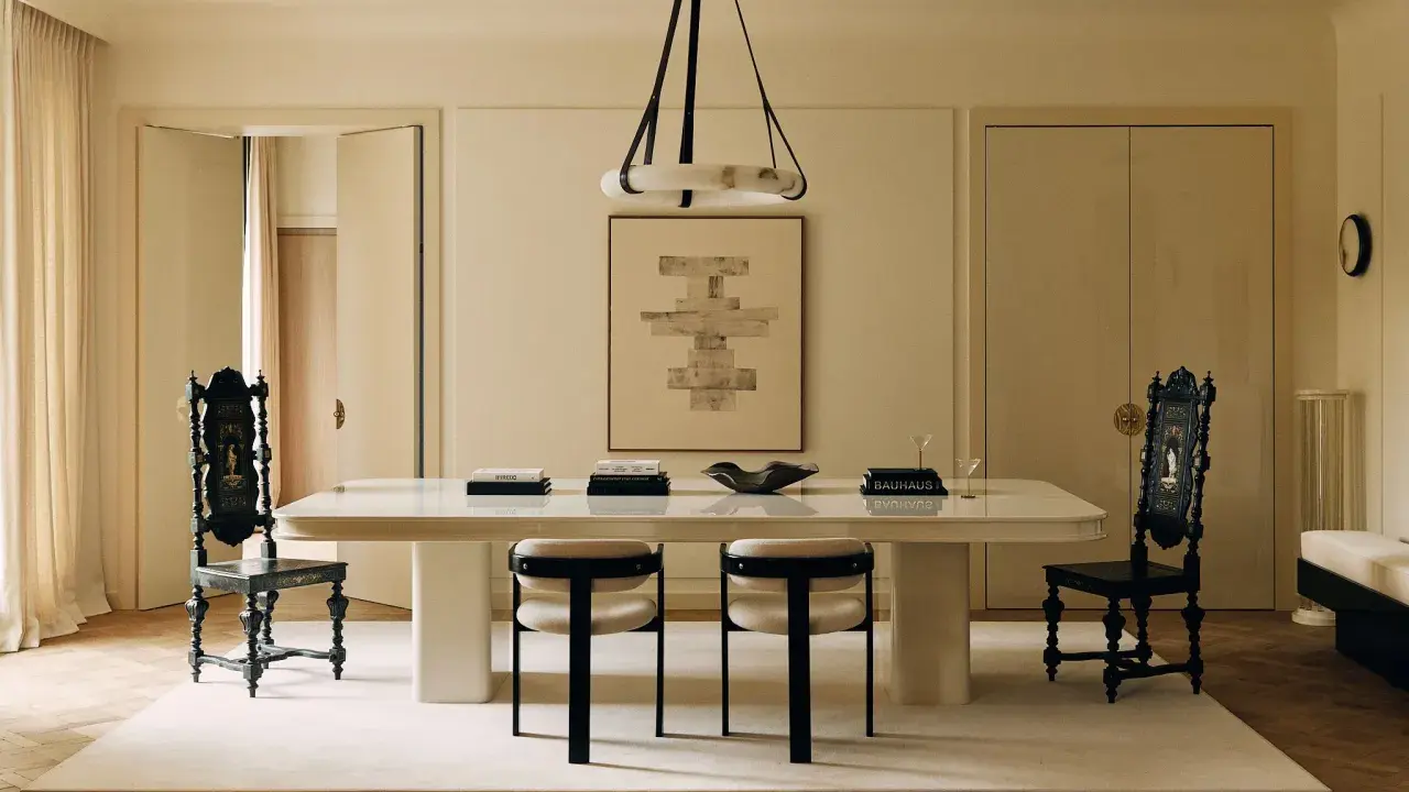 Comedor elegante con mesa blanca, sillas negras y una paleta de colores crema. Arte abstracto y cortinas suaves complementan el espacio.