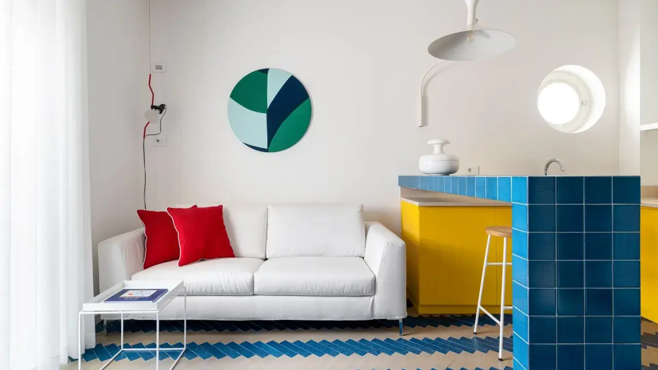 Sofá blanco, cojines rojos y suelo con **estilos de diseño** geométricos. Barra de cocina azul brillante y gabinetes amarillos vibrantes.