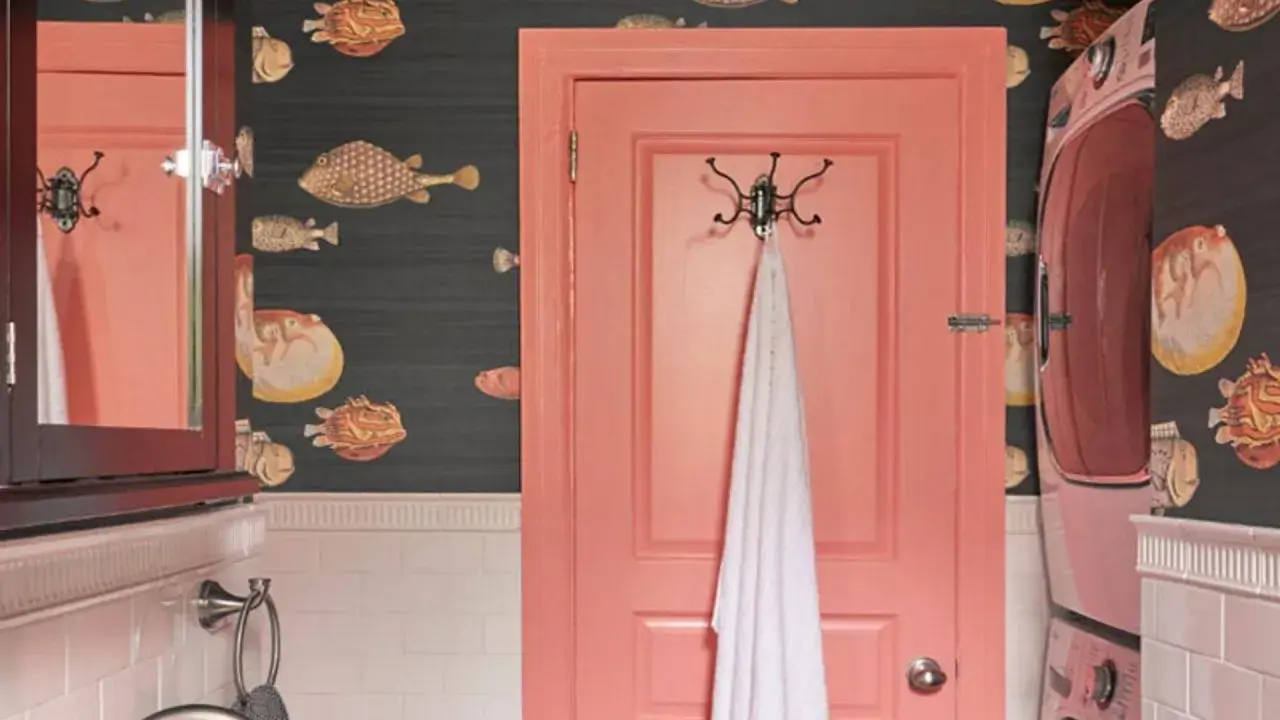 Un baño con papel tapiz de peces y **puertas de dos colores**: una rosa coral y otra de madera oscura con espejo.
