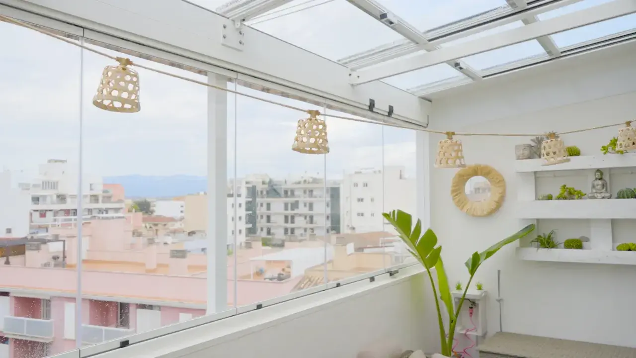 Un cerramiento ático con vistas urbanas, decorado con lámparas de mimbre y plantas.