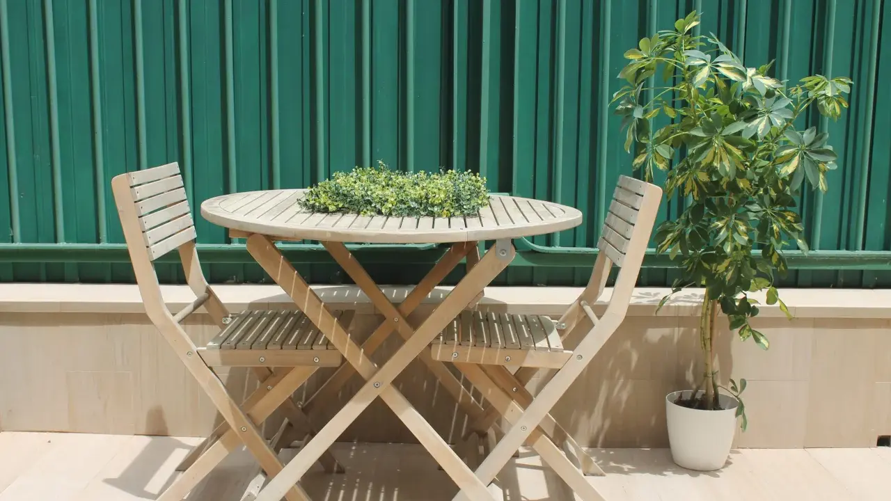 Conjunto de madera para dos personas en unas terrazas pequeñas con encanto. Una planta verde decora el rincón.