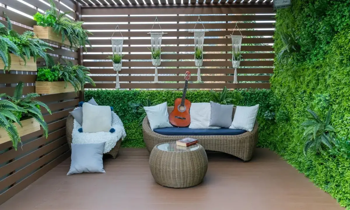 Terraza acogedora con muebles de mimbre, plantas colgantes y una pared verde. Ideal para relajarse, como cubrir una terraza con poco dinero.