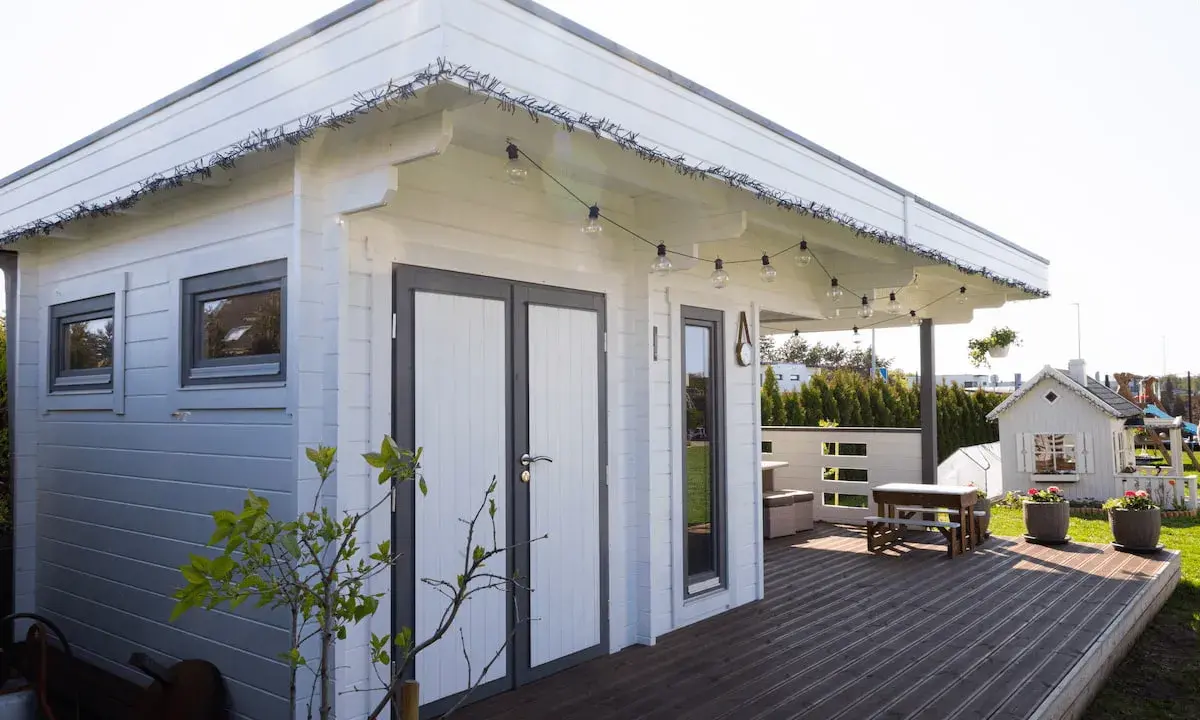 Una cabaña de madera con terraza, ideal para hacer una habitación en una terraza. Luces decorativas cuelgan del techo.