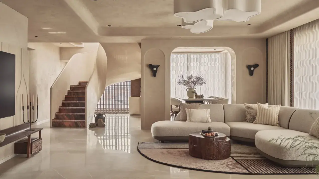 Salón con sofá curvo, mesa de centro de tronco y escaleras de mármol. Un espacio con estilo vanguardista y acabados orgánicos.