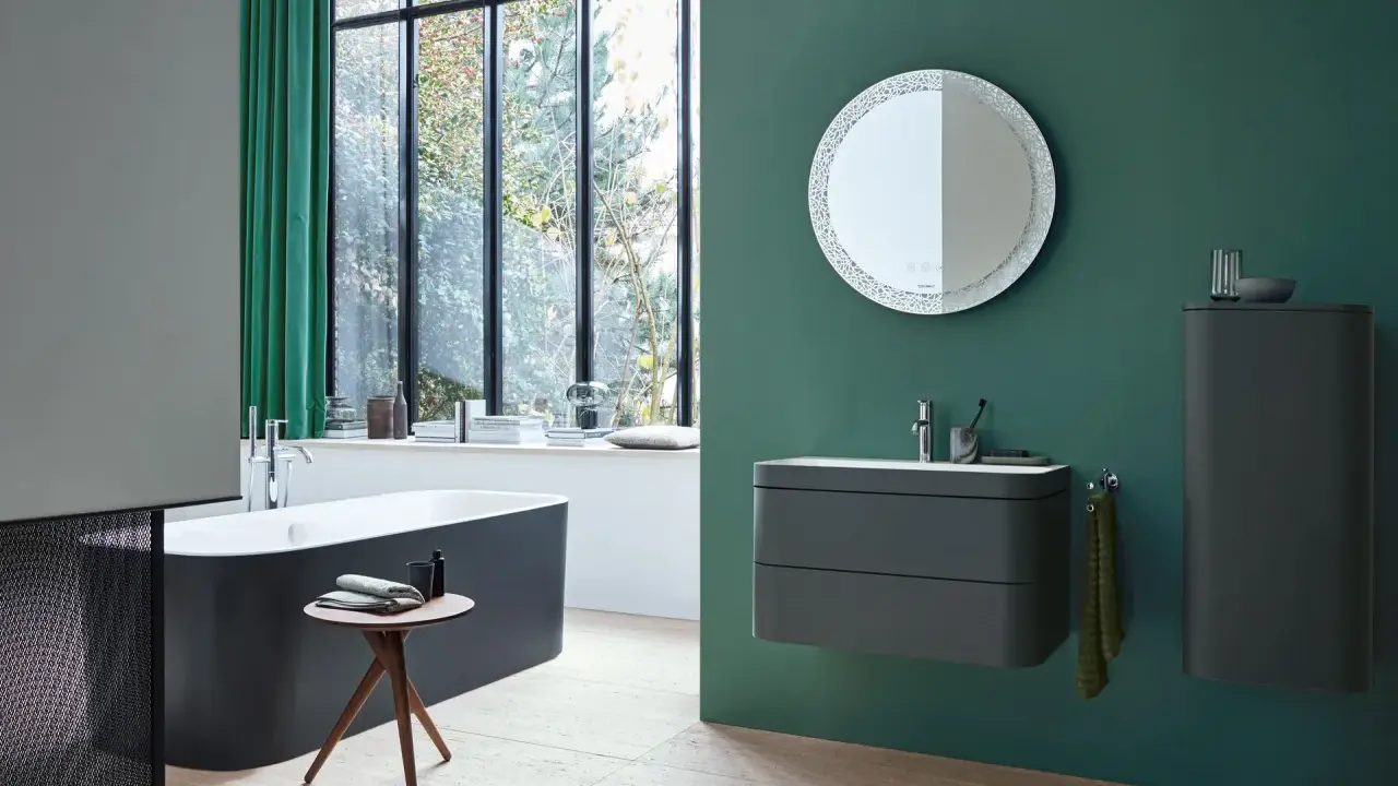 Un baño moderno con bañera oscura, lavabo flotante y espejo decorativo. La pared verde es un lienzo perfecto para pintar el baño.