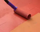 Rodillo pintando suelo de patio exterior con pintura roja, renovando el espacio.