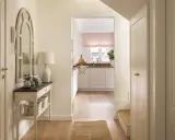Un recibidor luminoso con espejo arqueado, consola con cestas y una cocina al fondo. ¡Ideal para pintar recibidor y darle un toque fresco!