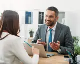 Un hombre sonriente, que parece ser un asesor energético, explica algo a una mujer en una oficina.