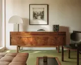 Elegante aparador de madera con **mid century decoracion**, lámpara de diseño, cuadro y silla de cuero.