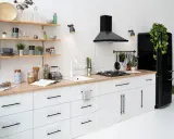Cocina moderna con gabinetes blancos y encimera de madera. El diseño para pintar cocinas es minimalista, con electrodomésticos negros y estantes de madera.