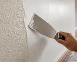 Mano aplica yeso con espátula para alisar paredes. Averigua cuanto vale alisar paredes para renovar tu hogar.