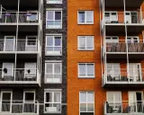 Fachada de edificio moderno con ladrillo naranja y oscuro, balcones blancos y ventanas. Un proyecto de reforma fachada casa que realza su estética.