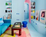 Salón pequeño con sofá azul, alfombra geométrica y estanterías llenas de objetos. Los colores pastel y vibrantes son ideales como colores para pintar salones pequeños.