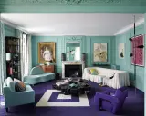 Sala de estar con paredes turquesas y alfombra morada. Muebles modernos y un retrato clásico crean un espacio amplio, ideal para aprender como pintar una habitacion para que se vea mas grande.