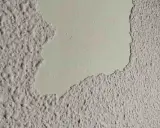Detalle de pared con gotelé descascarillado, mostrando la capa inferior lisa. Ideal para aprender como quitar gotele.