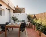 Acogedora terraza de 25 metros cuadrados con mesa de madera, sillas negras, sofá, plantas y luces decorativas.