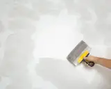 Mano con espátula trabajando en pared rugosa, como quitar pintura.