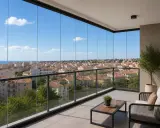 Balcón con una **fachada de cristal** que ofrece vistas panorámicas de una ciudad costera bajo un cielo azul.