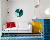 Sofá blanco, cojines rojos y suelo con **estilos de diseño** geométricos. Barra de cocina azul brillante y gabinetes amarillos vibrantes.
