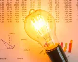 Bombilla incandescente sobre gráficos y tablas. ¿Qué es la tarifa indexada luz? Representa la fluctuación de precios en el mercado eléctrico.