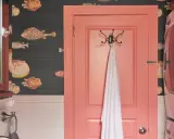 Un baño con papel tapiz de peces y **puertas de dos colores**: una rosa coral y otra de madera oscura con espejo.
