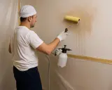 Hombre con rodillo y pulverizador, trabajando para quitar gotele plástico de la pared.