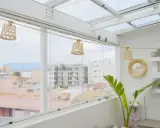 Un cerramiento ático con vistas urbanas, decorado con lámparas de mimbre y plantas.