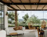 Terraza minimalista con sofá blanco, sillas colgantes de mimbre y vistas a un paisaje verde.