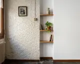 Un rincón con paredes lisas y otra con gotele, un retrato familiar, estanterías con libros y una planta.