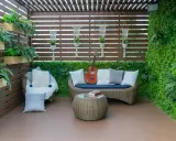 Terraza acogedora con muebles de mimbre, plantas colgantes y una pared verde. Ideal para relajarse, como cubrir una terraza con poco dinero.