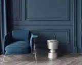 Elegante sillón azul junto a una mesa auxiliar plateada, con cortinas a juego y detalladas molduras en paredes de tono oscuro.