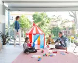 Familia divirtiéndose en una terraza decorada para niños con una carpa de circo y juegos.