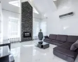 Un moderno salón con un sofá gris oscuro, chimenea de piedra y suelo de mármol blanco.