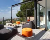 Cómodo balcón terraza con sillones, pufs naranjas y mesas bajas, con vistas a la ciudad.