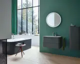 Un baño moderno con bañera oscura, lavabo flotante y espejo decorativo. La pared verde es un lienzo perfecto para pintar el baño.