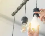 Manos cambian una bombilla LED por una incandescente en una lámpara colgante, actualizando la luz del hogar.