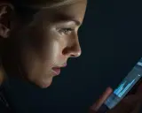 Mujer revisa su móvil, buscando información para cambiar compañía luz. La pantalla ilumina su rostro pensativo.