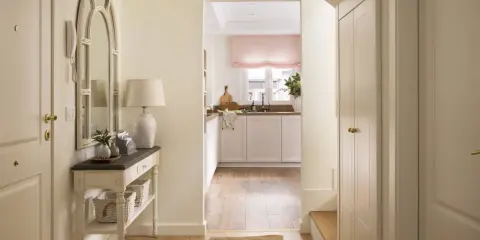Un recibidor luminoso con espejo arqueado, consola con cestas y una cocina al fondo. ¡Ideal para pintar recibidor y darle un toque fresco!