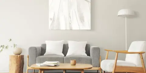 Un cuadro de hoja en tonos claros decora la pared, complementando el estilo zen de los cuadros feng shui dormitorio. Sofá gris, sillón blanco y mesa de centro de madera.